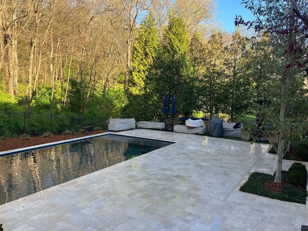 Modern backyard pool surrounded by natural greenery and elegant stone patio.