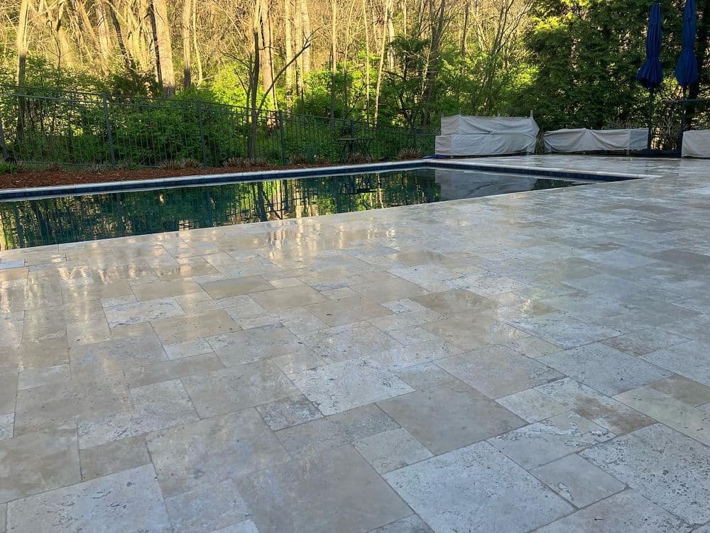 Tranquil backyard pool with tiled patio and lush greenery in the background.