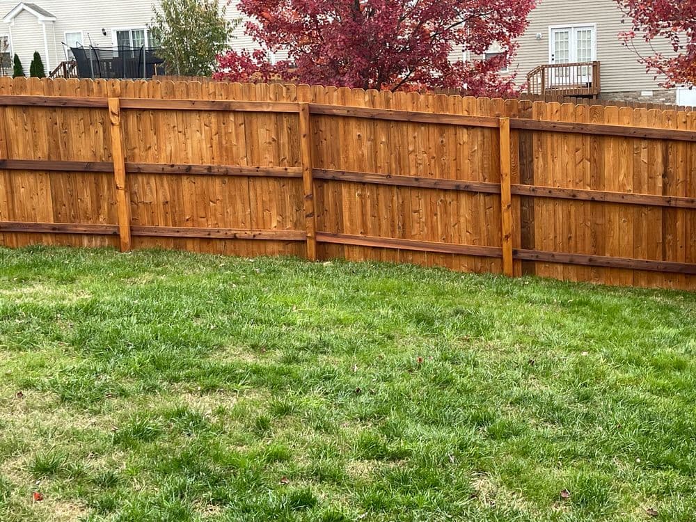Wooden fence enclosing a green lawn with colorful fall foliage in the background.