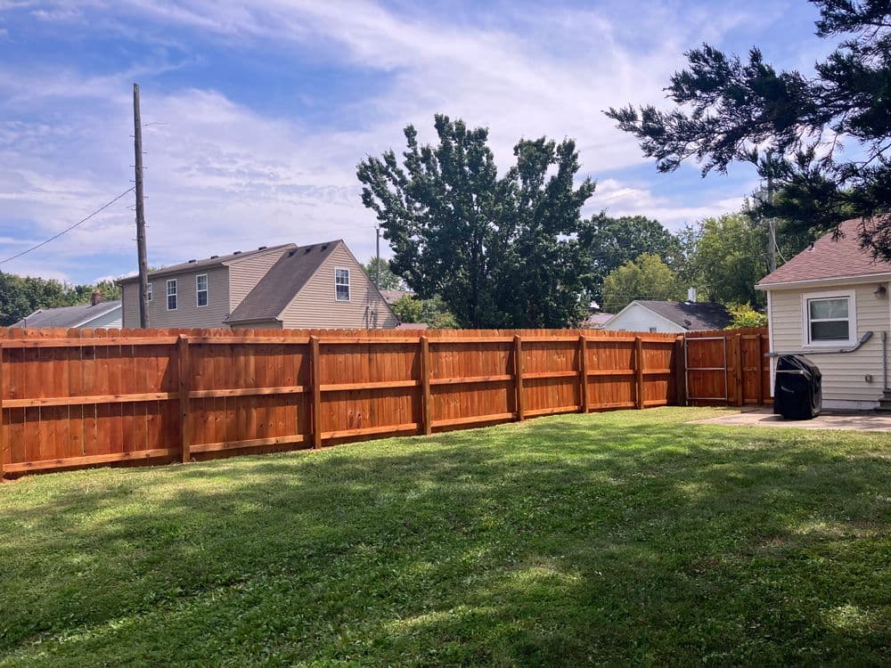 Wooden privacy fence in a sunny backyard with green grass and nearby houses.