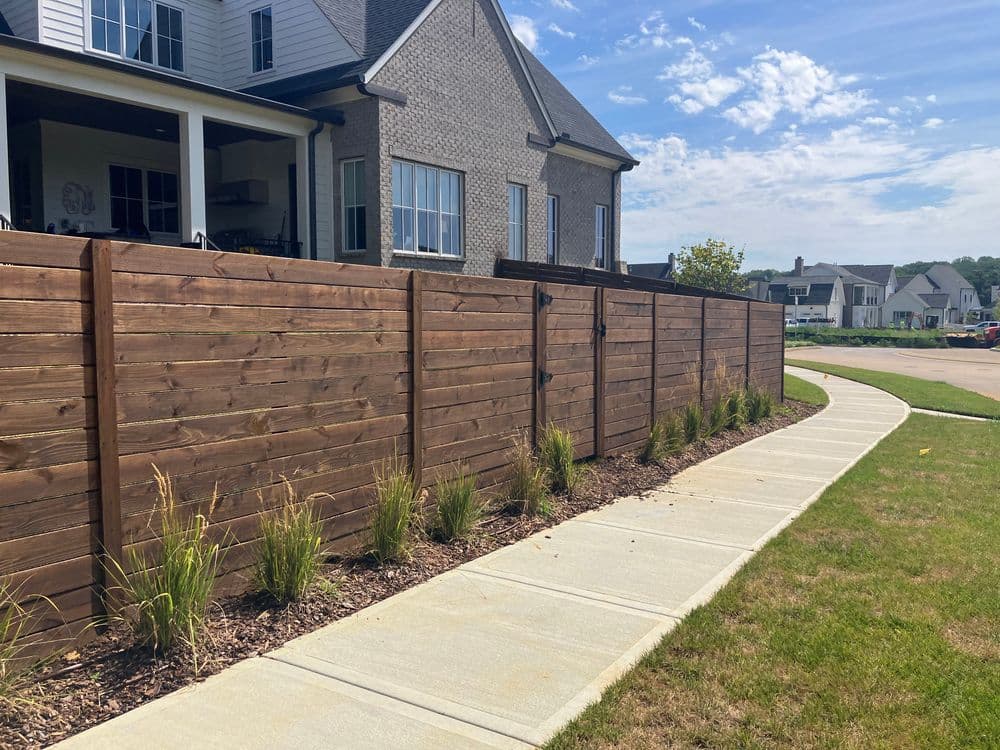 Wooden privacy fence alongside a concrete walkway and landscaped grass in a residential area.