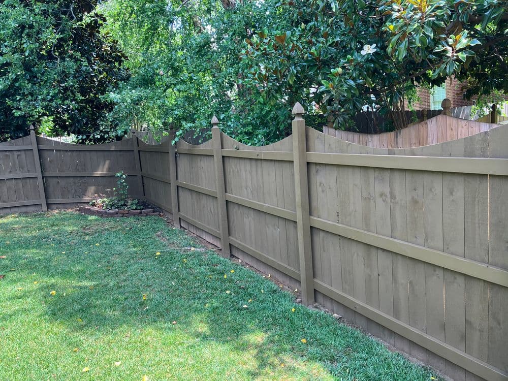 Wooden privacy fence in lush green backyard, surrounded by trees and grass.