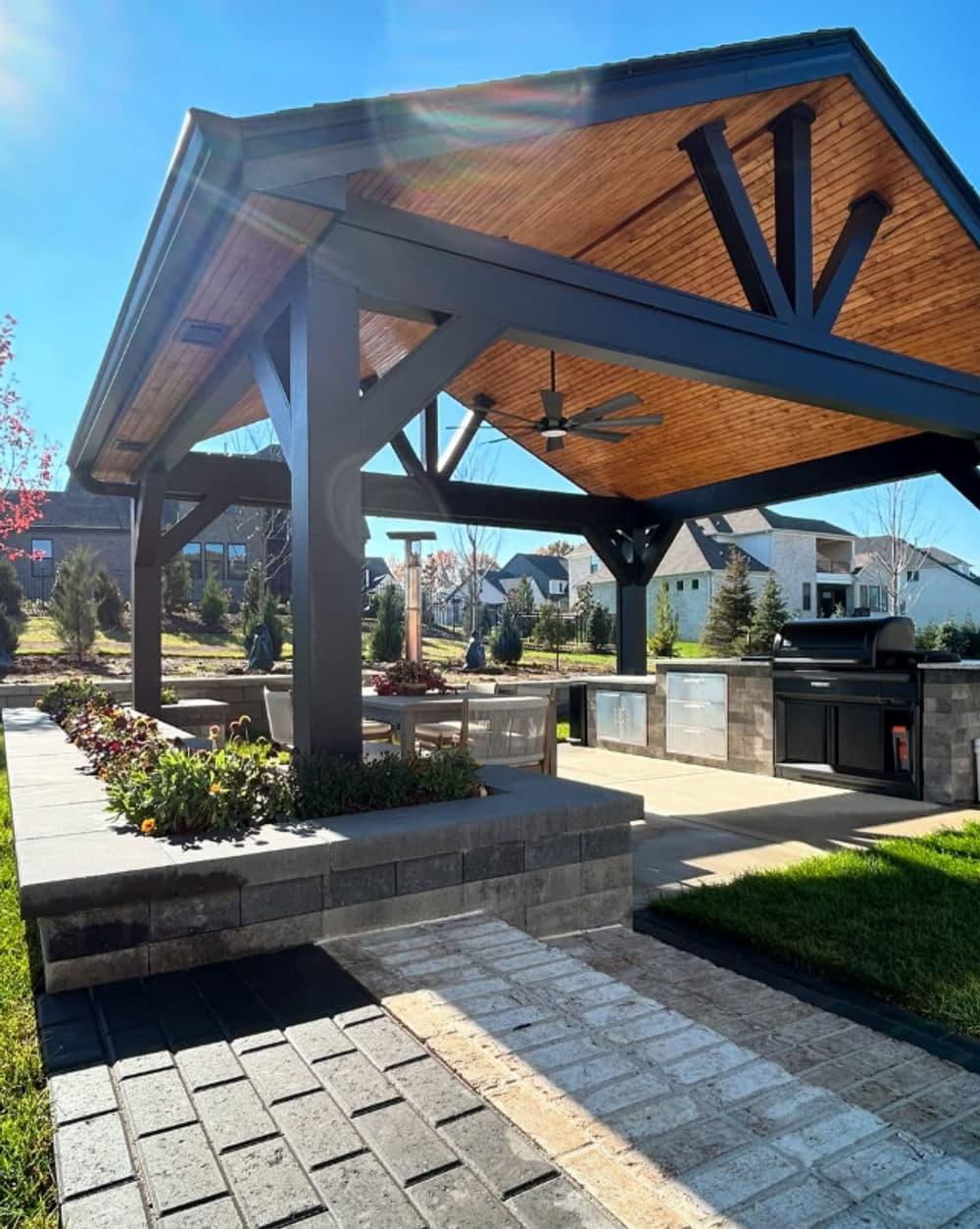 Modern outdoor kitchen pavilion with seating area, grill, and landscaped garden.