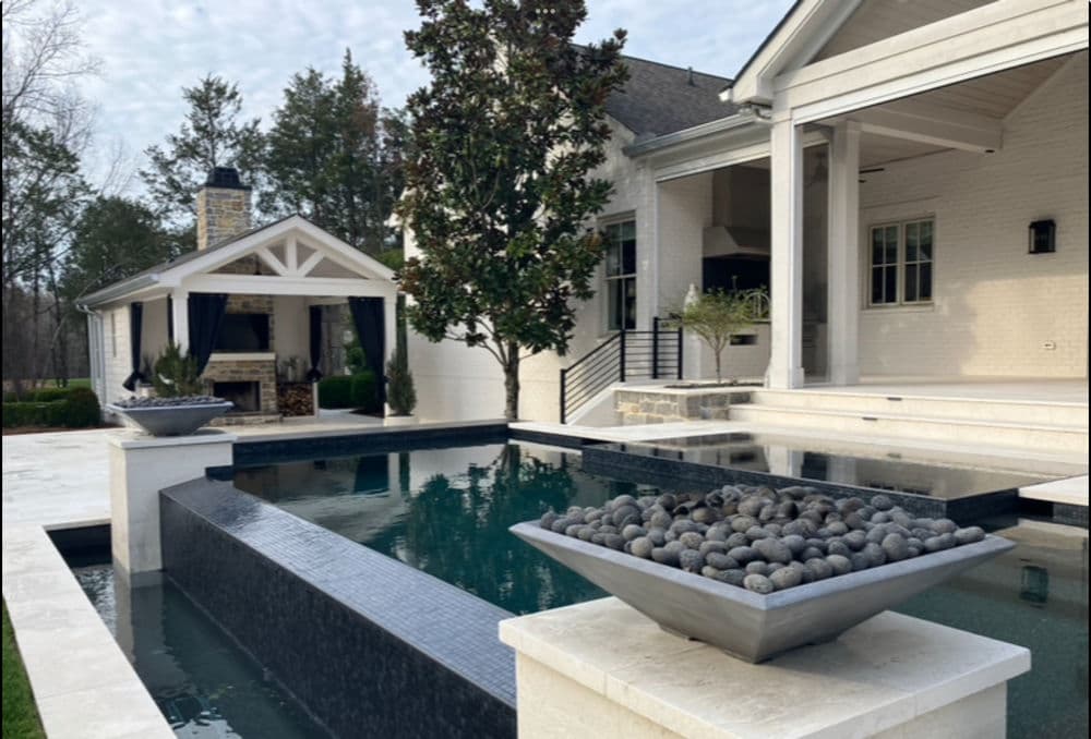 Modern outdoor pool with sleek marble design and decorative stone planters in luxury home setting.