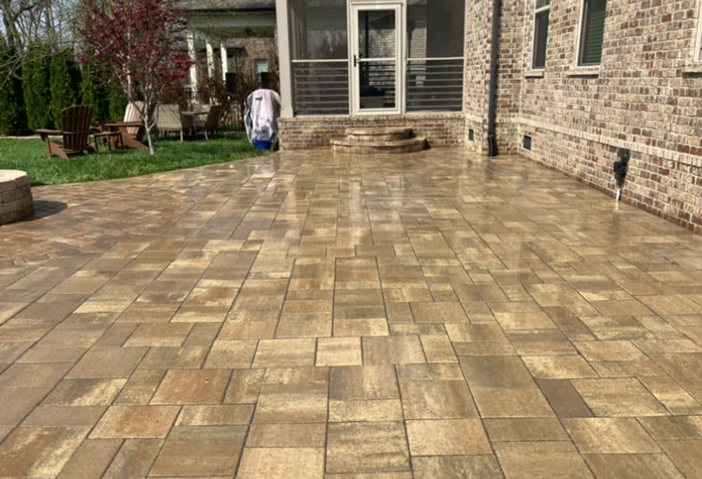 Cleaned patio with patterned stone pavers, person walking towards house in background.