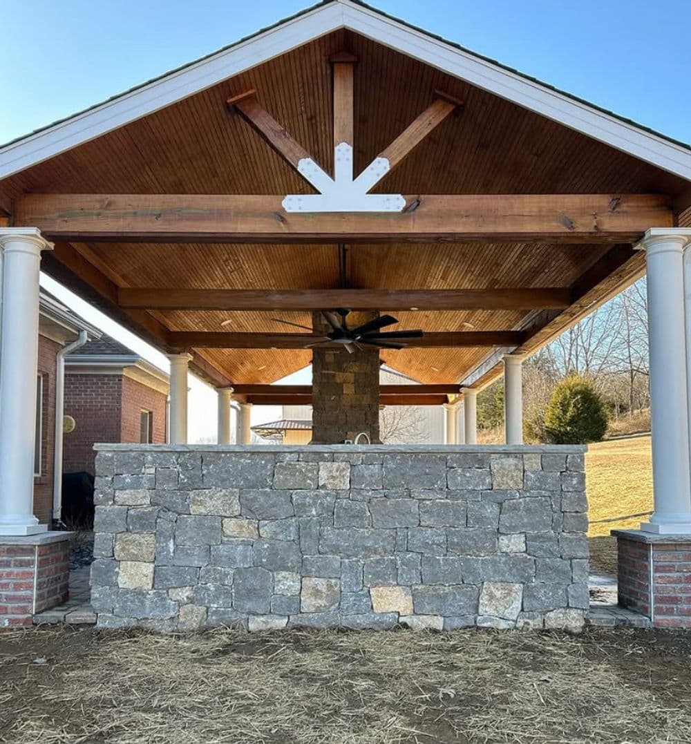 Stylish outdoor pavilion with stone walls and wooden ceiling, ideal for gatherings.