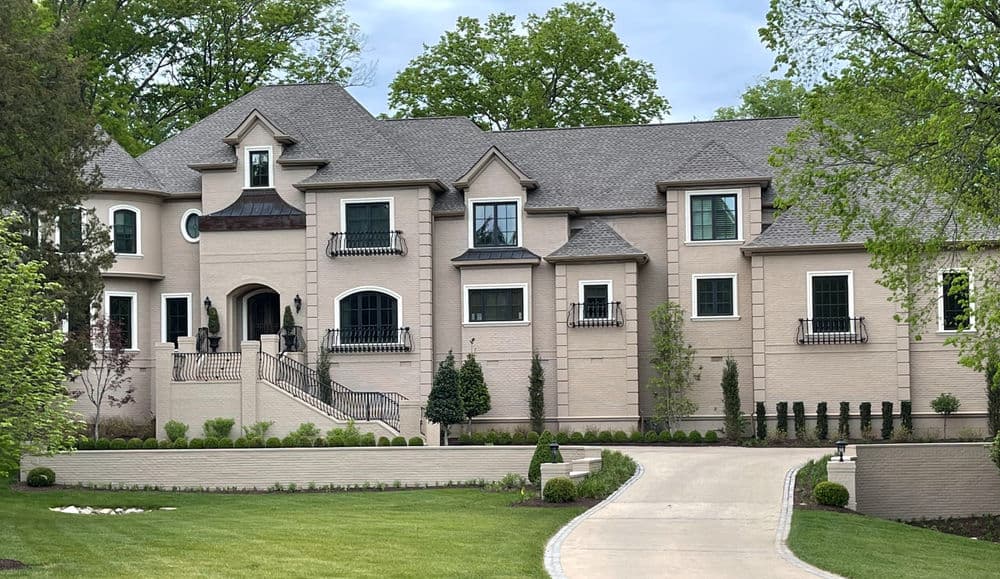 Elegant brick mansion with front staircase, manicured lawn, and lush greenery.
