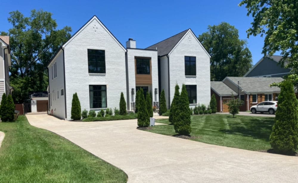 Modern two-story white brick home with large windows and landscaped driveway.