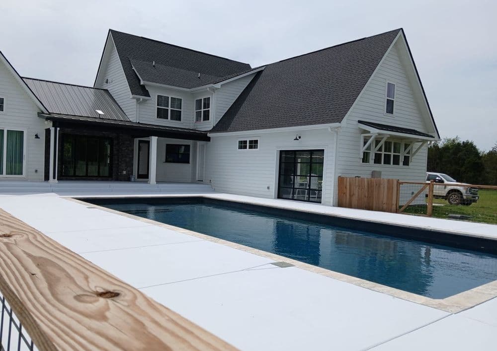 Modern home with a pool, featuring a spacious patio and lush green surroundings.