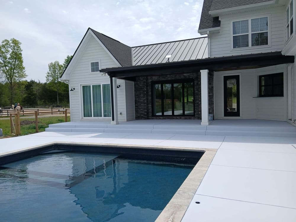 Modern home exterior with a pool, patio area, and lush greenery in the background.