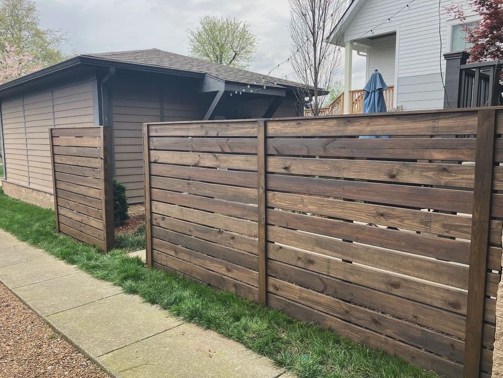 Modern wooden fence with horizontal slats in a residential backyard setting.