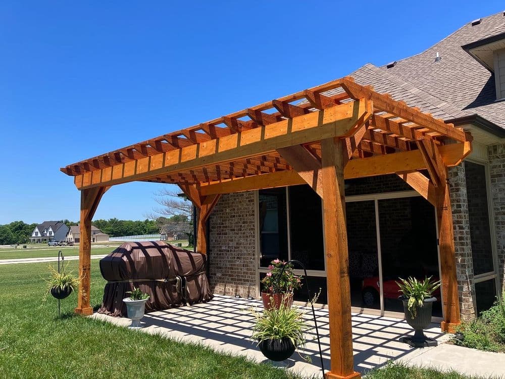 Wooden pergola with a grill and potted plants in a sunny backyard setting.