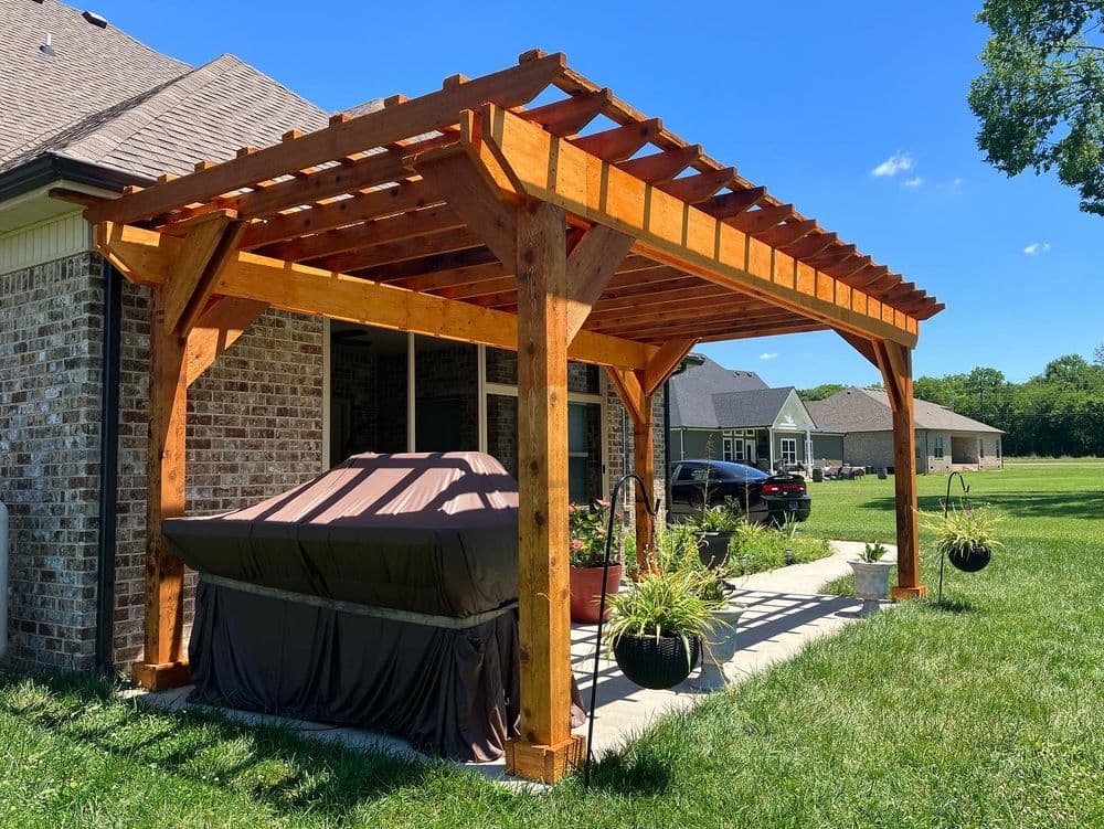Wooden pergola over a hot tub in a backyard with green grass and blue sky.