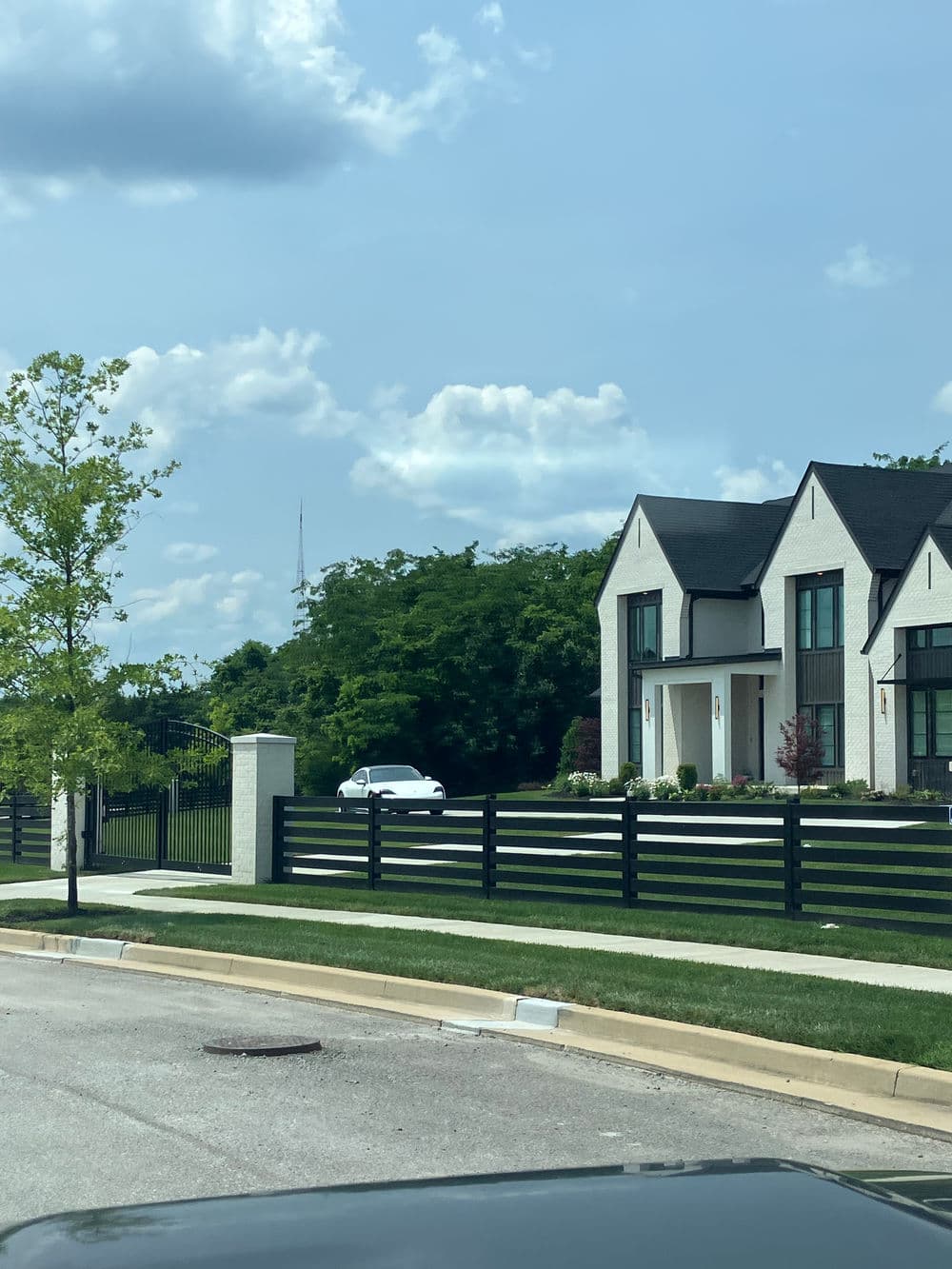 Modern home with a black fence, green landscaping, and cloudy sky in the background.