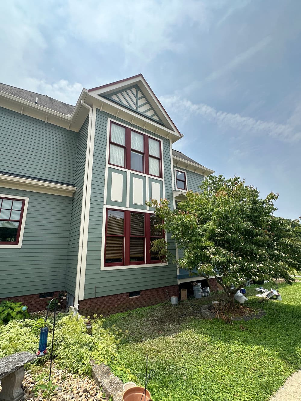 Victorian-style house exterior with green siding, red windows, and lush garden.