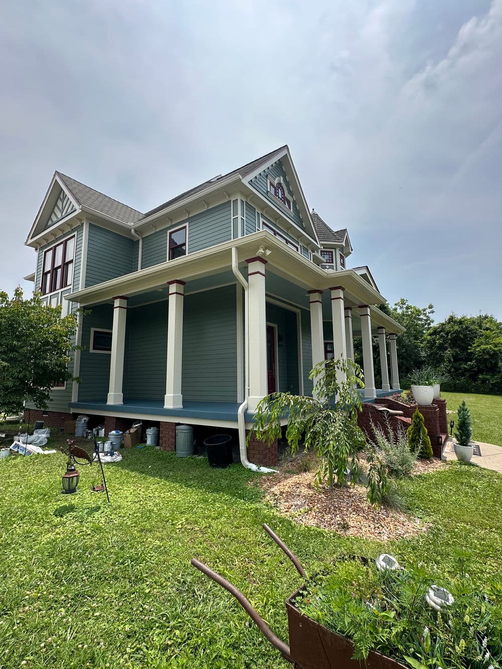 Victorian-style blue house with porch, garden, and green lawn under a cloudy sky.