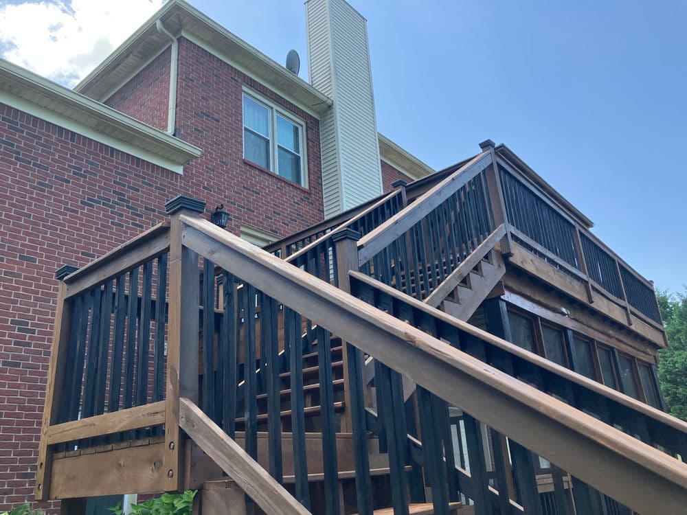 Wooden deck and stairs leading to a brick house under a clear blue sky.