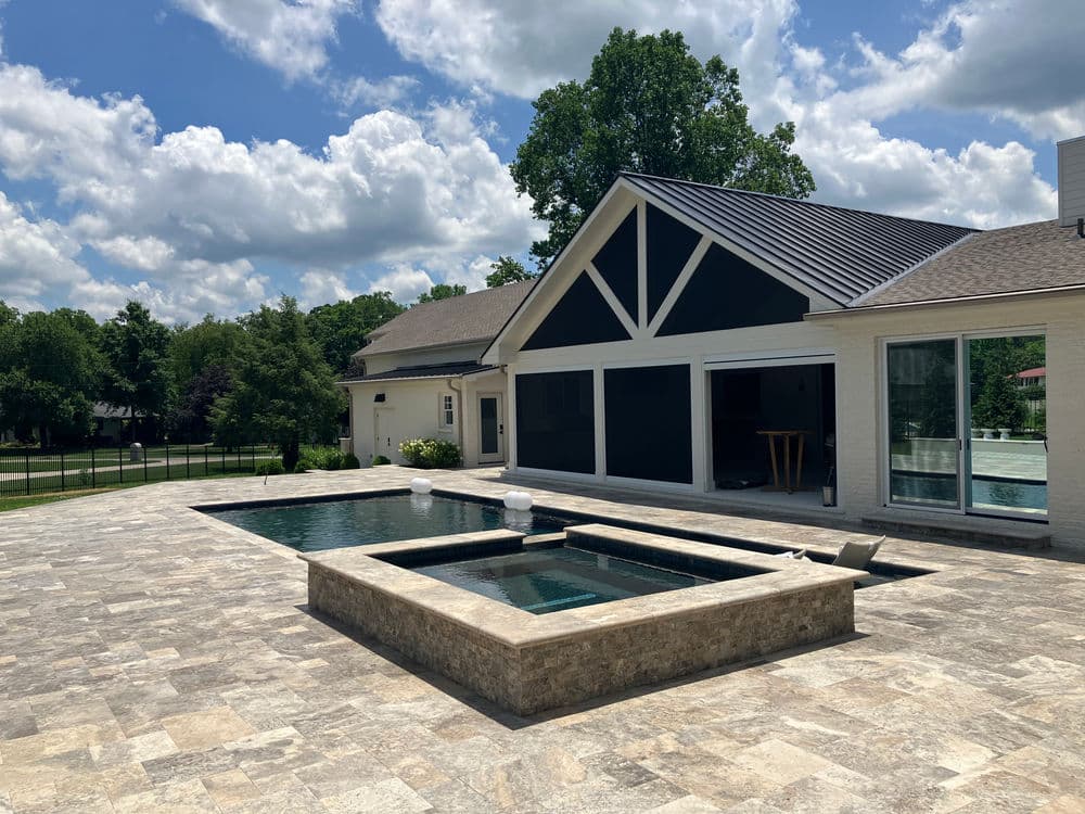 Modern backyard with a stone patio, two pools, and a stylish house under a cloudy sky.