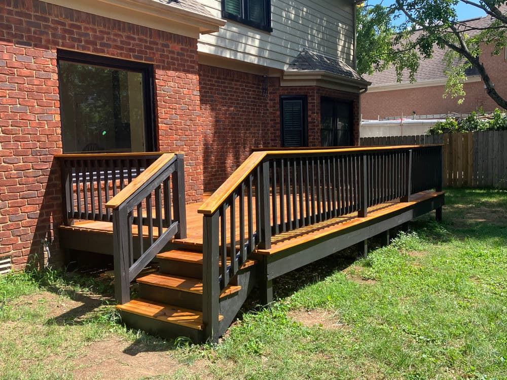 Newly built wooden deck with railing and stairs, connecting to a brick house and grassy yard.