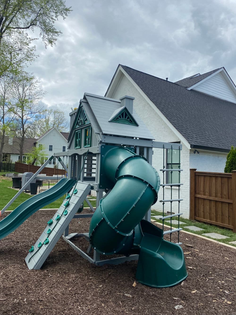 Colorful backyard playground with slide and spiral slide by a house, surrounded by mulch.