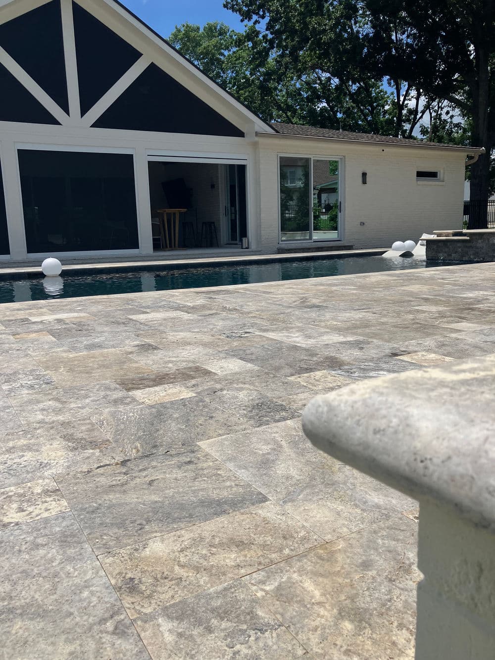 Modern outdoor pool with stone patio and stylish house in background, sunny day.