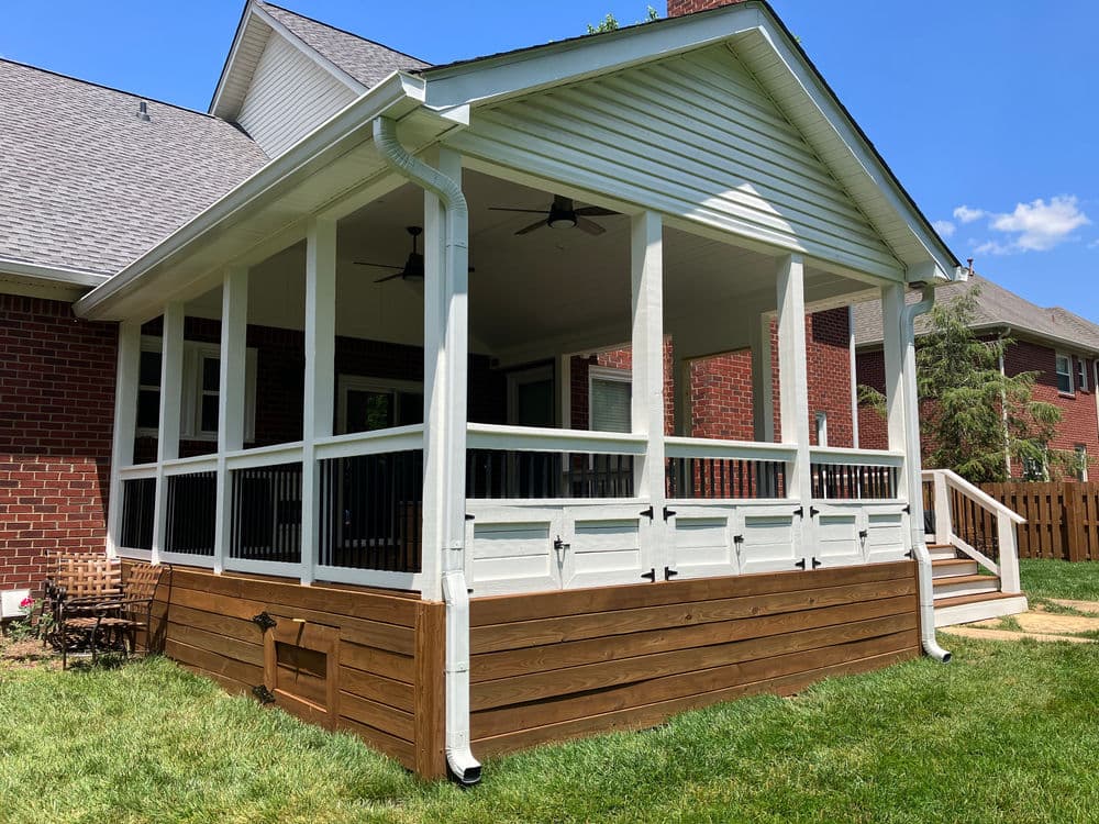 Newly constructed backyard porch with white railing, wooden base, and green lawn.