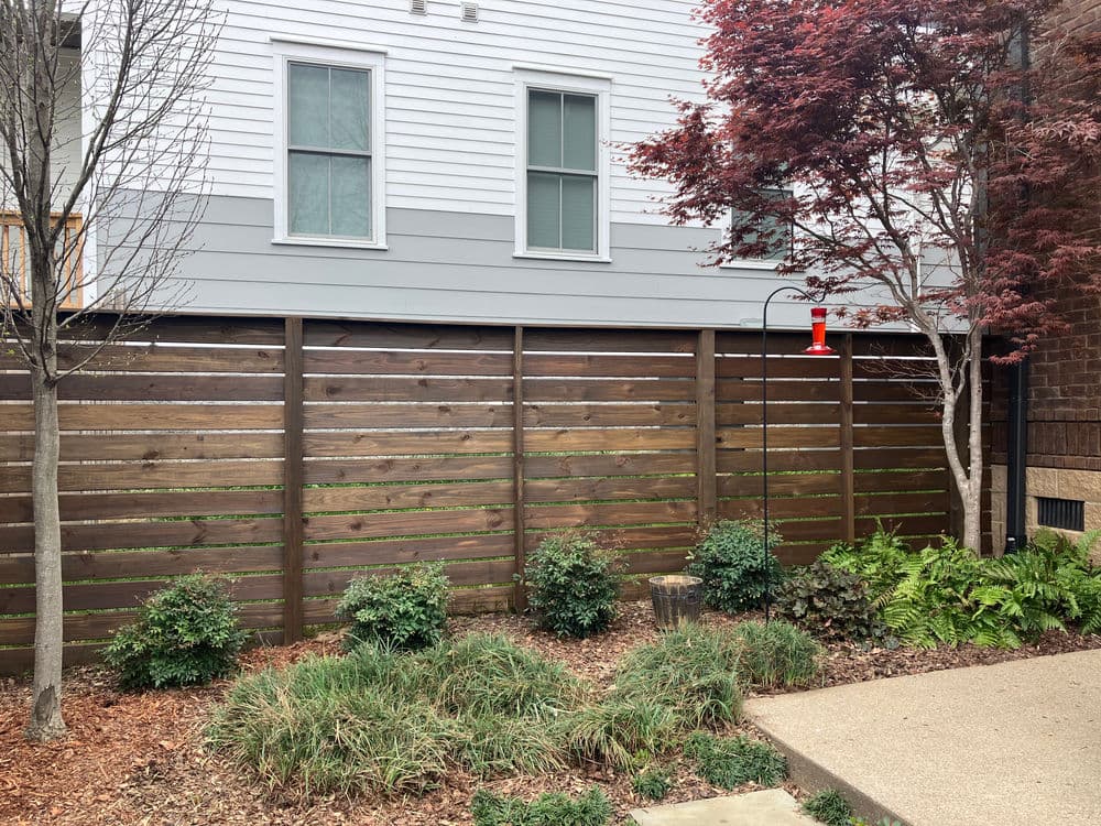 Modern wooden fence in a landscaped yard with shrubs and a hummingbird feeder.