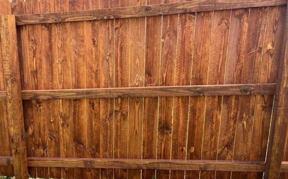 Newly stained wooden fence with rich brown color and vertical planks. Ideal for backyard privacy.