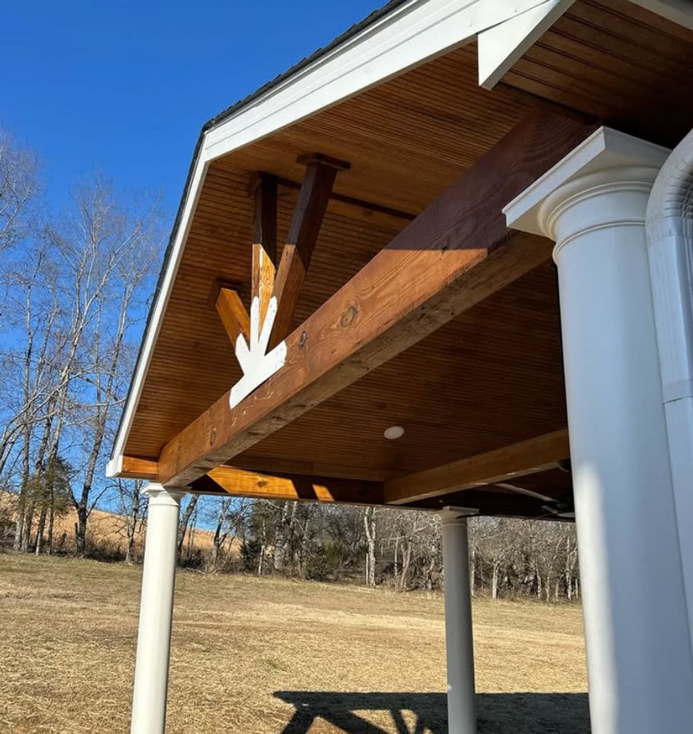 Wooden beams and white accents under a porch roof, showcasing rustic outdoor architecture.