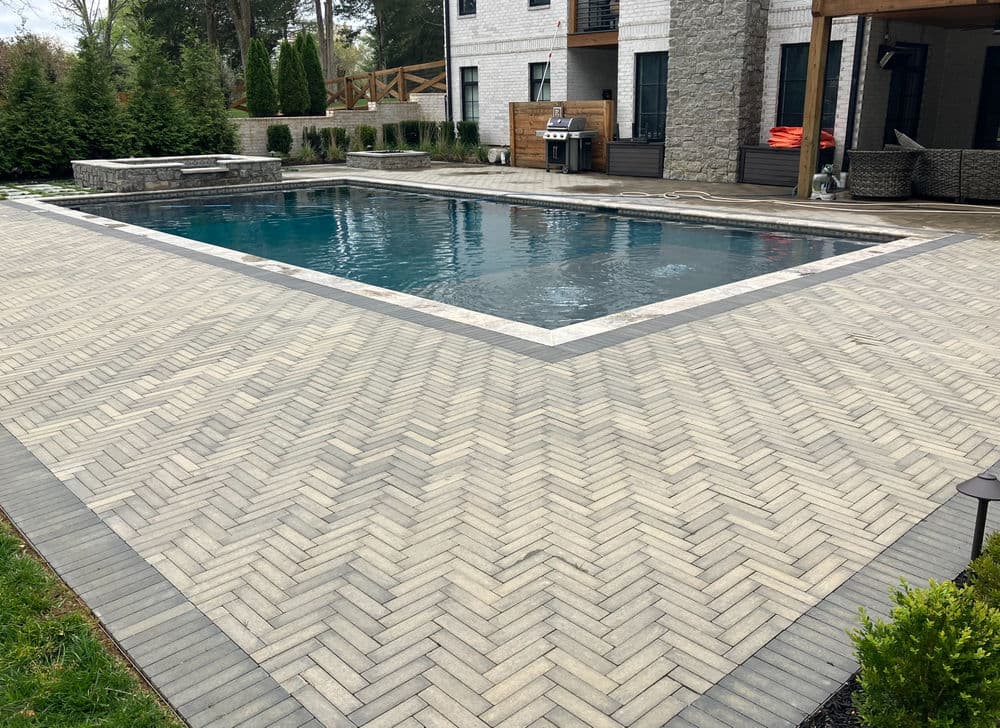 Modern backyard oasis with a pool, herringbone pavers, and landscaped greenery.