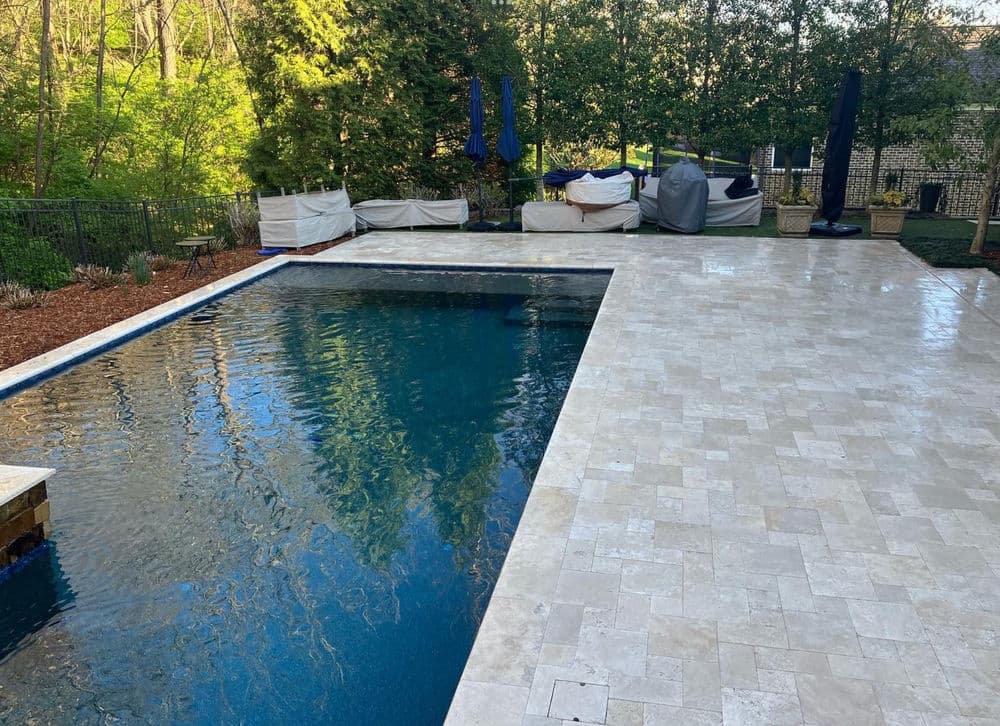 Stylish outdoor pool surrounded by stone patio and lush greenery in a residential garden.