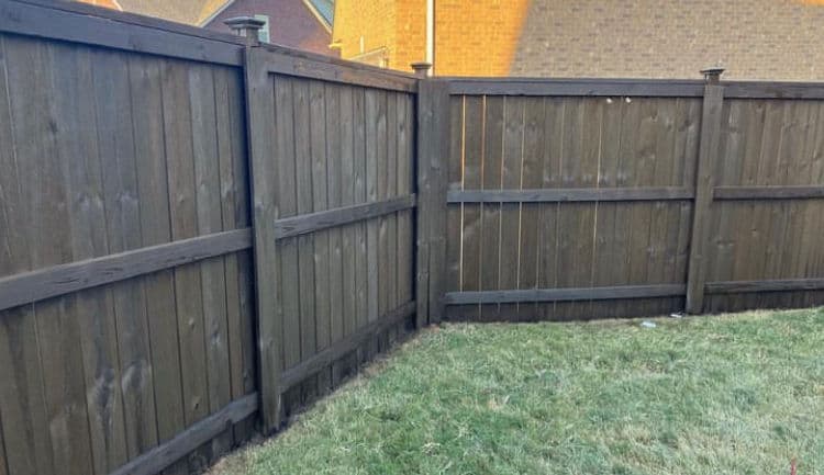 Wooden fence with vertical slats, corner view, on grassy lawn and suburban backdrop.