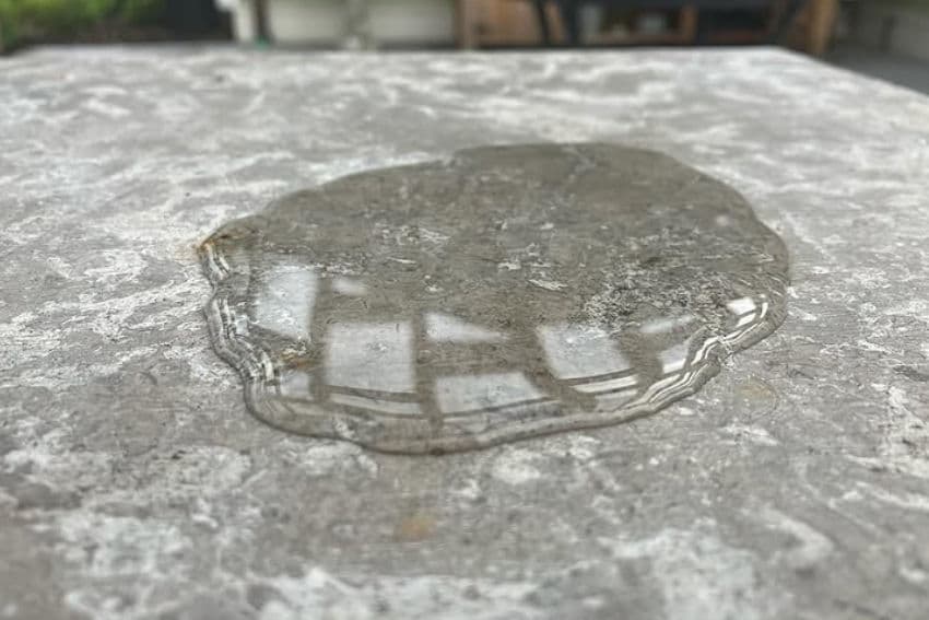 Water puddle on a textured stone surface reflecting surroundings.