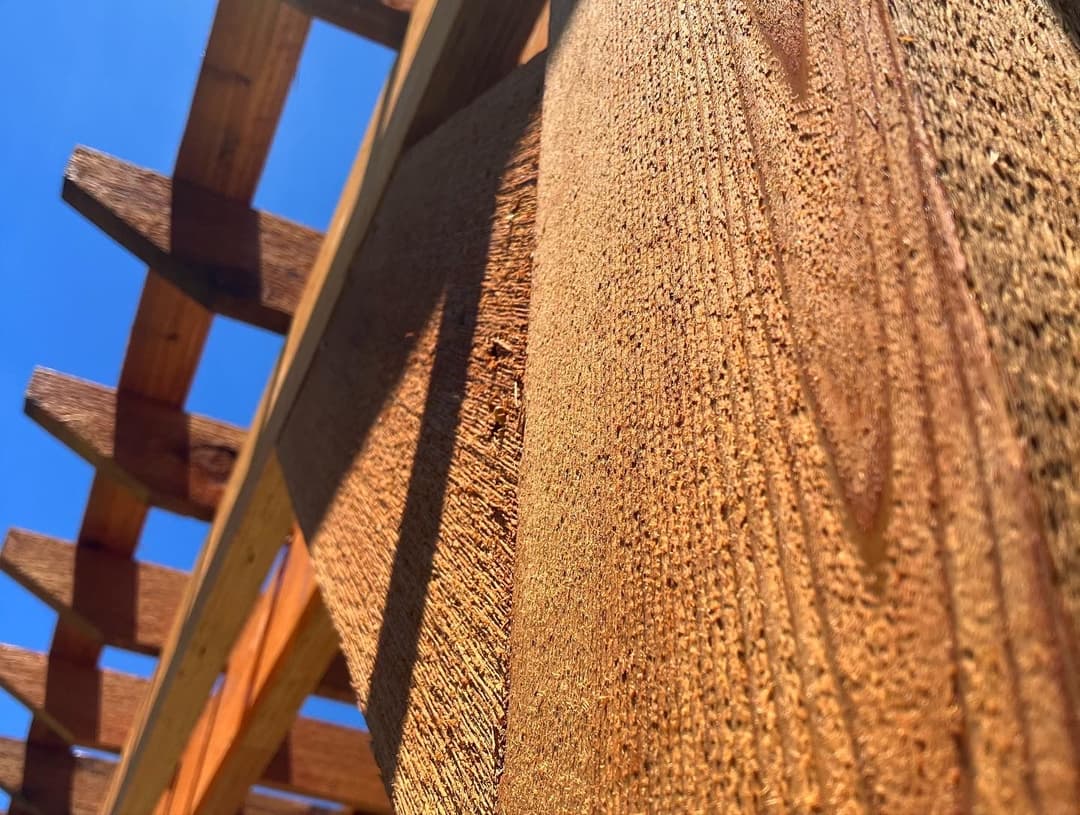 Close-up of textured wood beam under a pergola against a clear blue sky.