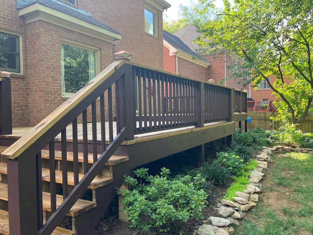 Backyard deck with wooden railing surrounded by greenery and stone pathway.