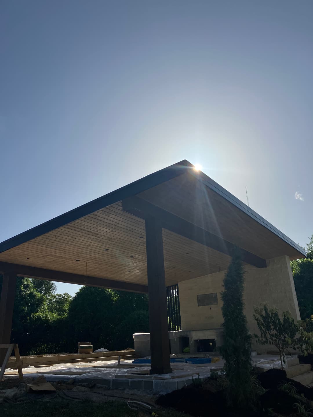 Modern outdoor pavilion with wooden ceiling, sunlight shining, and landscaped surrounding.