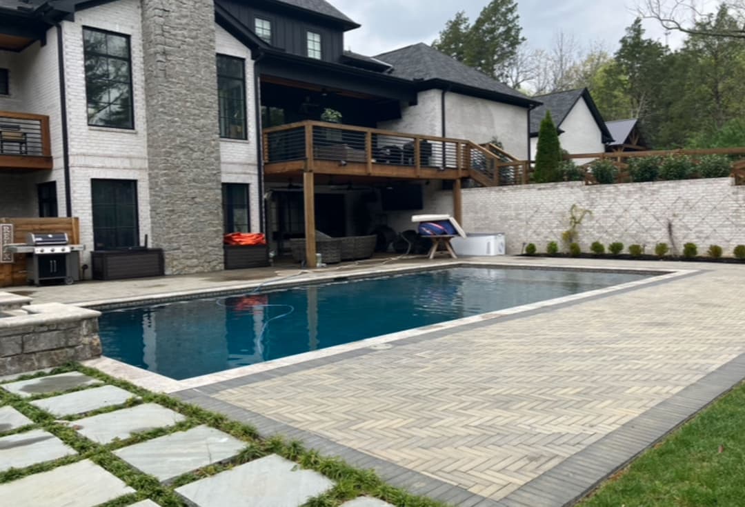 Modern backyard featuring a luxurious swimming pool, stone patio, and stylish home exterior.