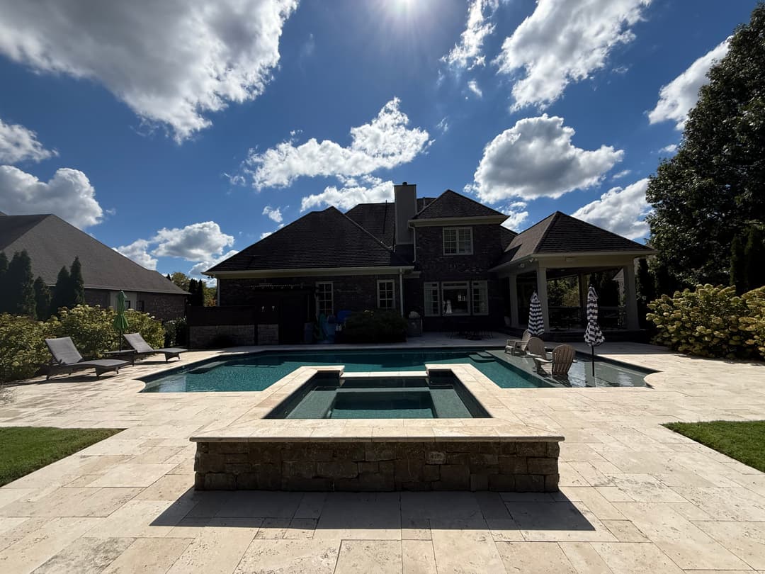 Luxury backyard with a pool, spa, and modern home under a blue sky with fluffy clouds.
