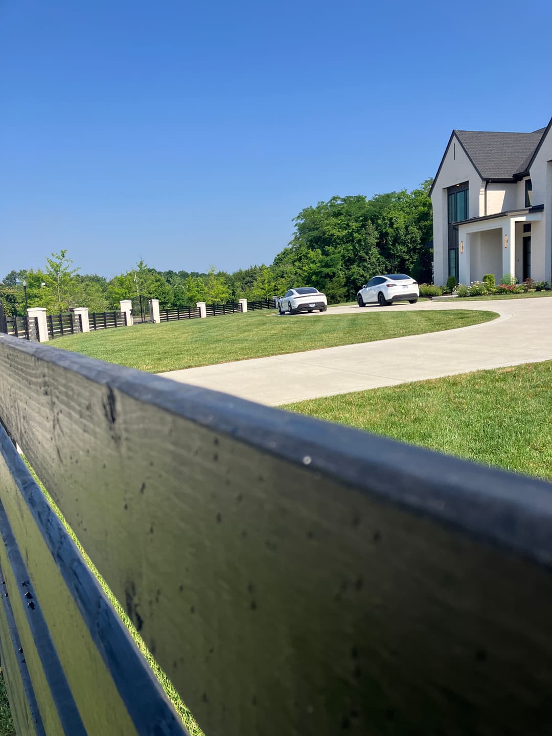 Modern house with two white cars parked on a circular driveway, green lawn and clear blue sky.
