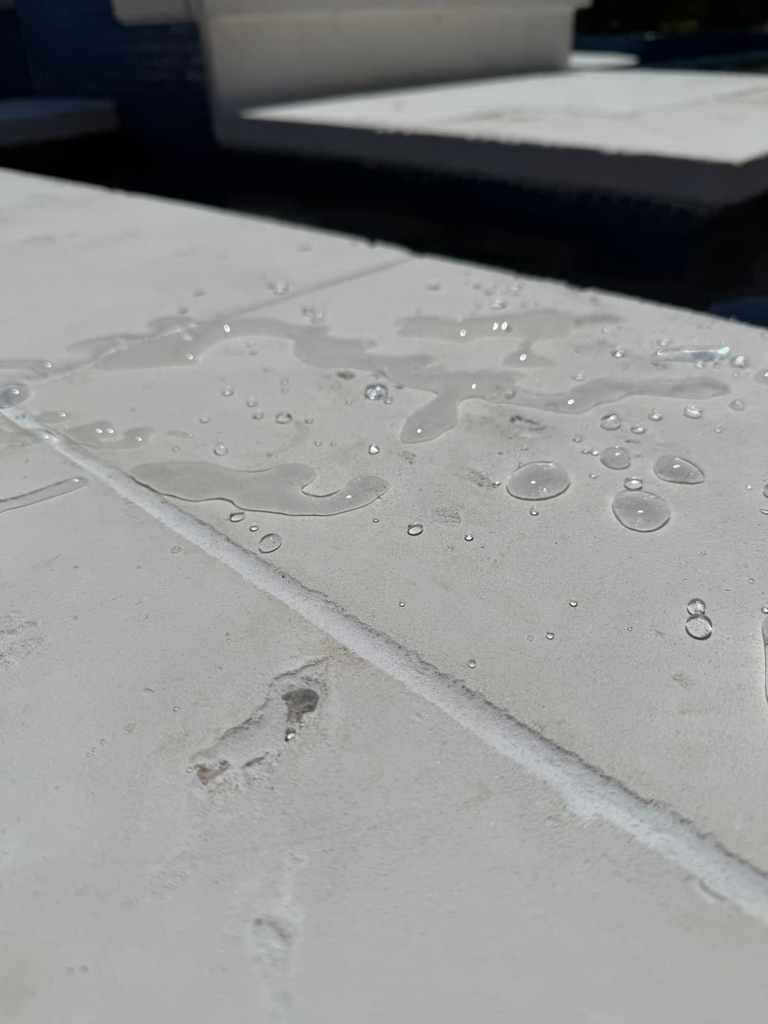 Water droplets on a textured white tile surface under bright sunlight.