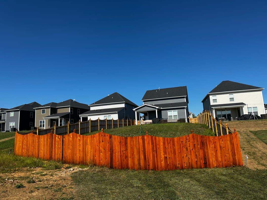 Vibrant orange wooden fence in front of modern suburban homes under a clear blue sky.