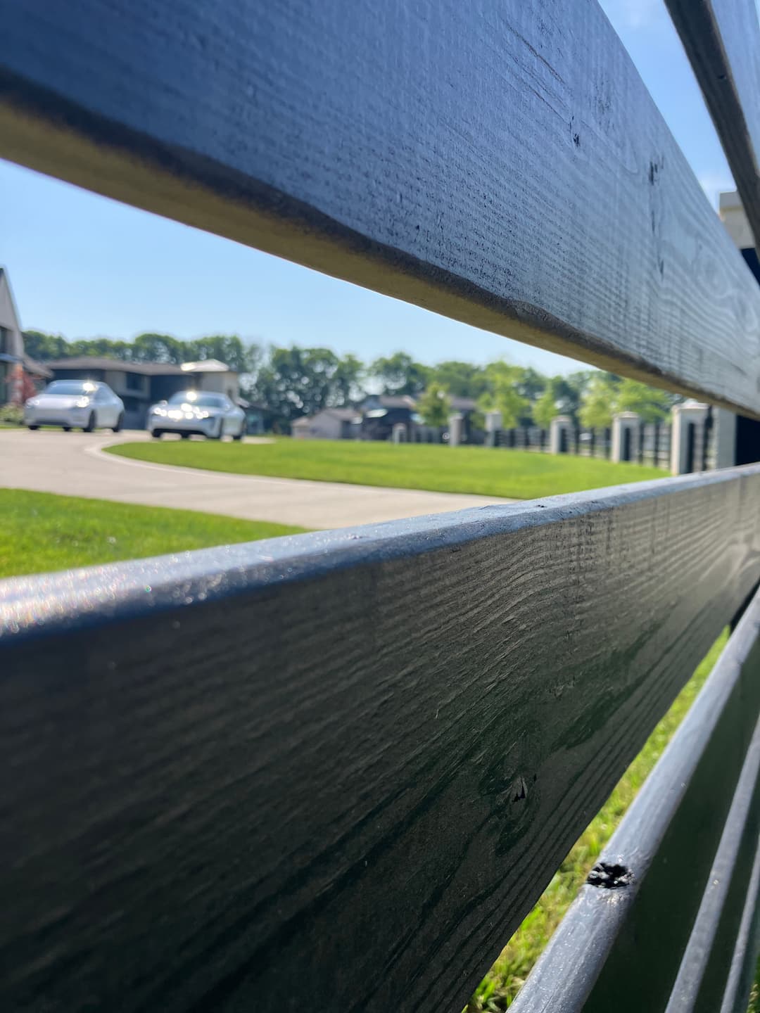 Close-up of a wooden fence with a view of a green lawn and houses in the background.