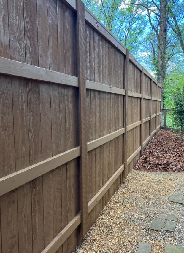 Wooden privacy fence along a gravel pathway with trees in the background.