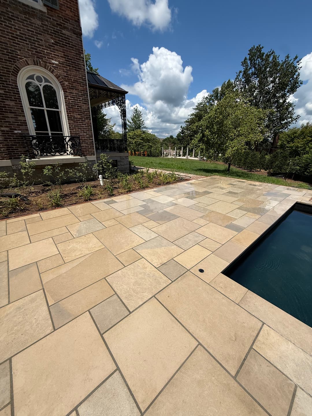 Elegant patio with stone pavers beside a pool, lush greenery, and a charming gazebo.