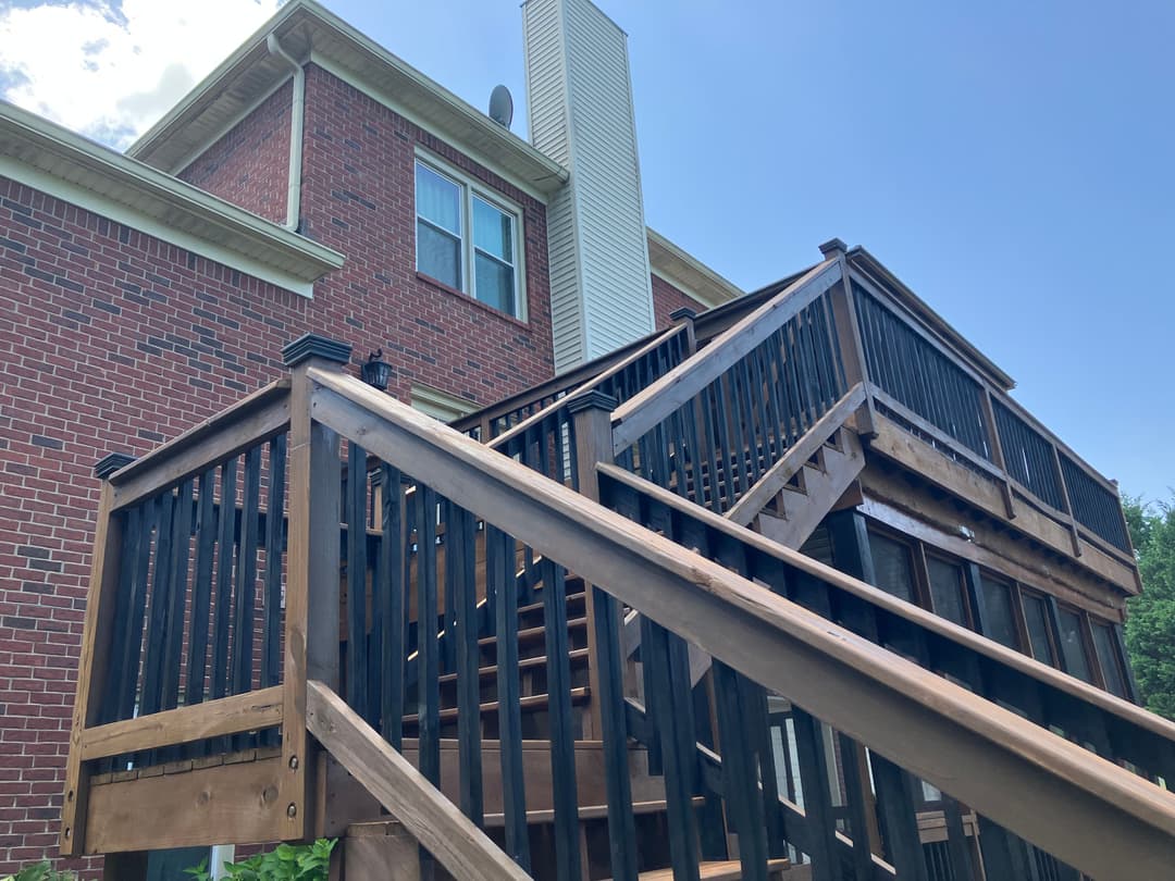 Wooden deck and stairs leading to a brick house, blue sky in the background.
