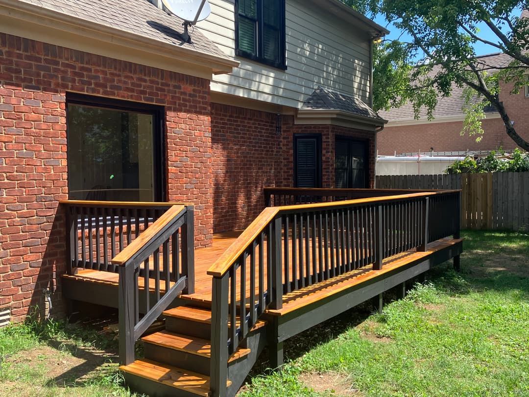 Newly built wooden deck with black railing and brick house background in a sunny backyard.