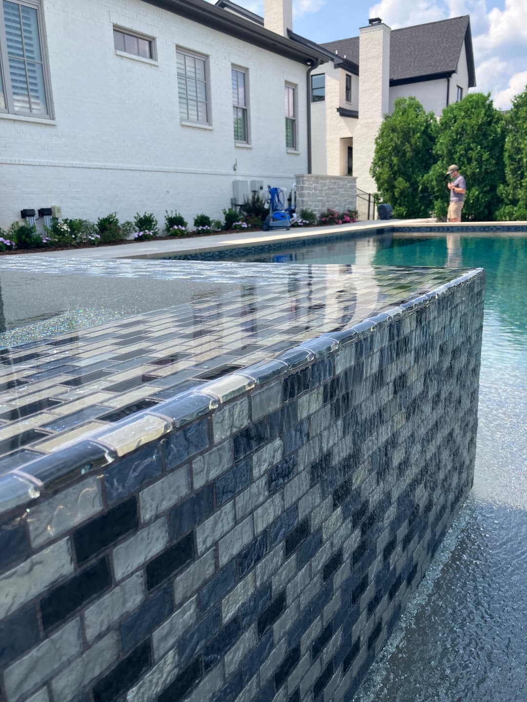 Modern backyard pool with a stone fountain feature and a person enjoying the scenery.