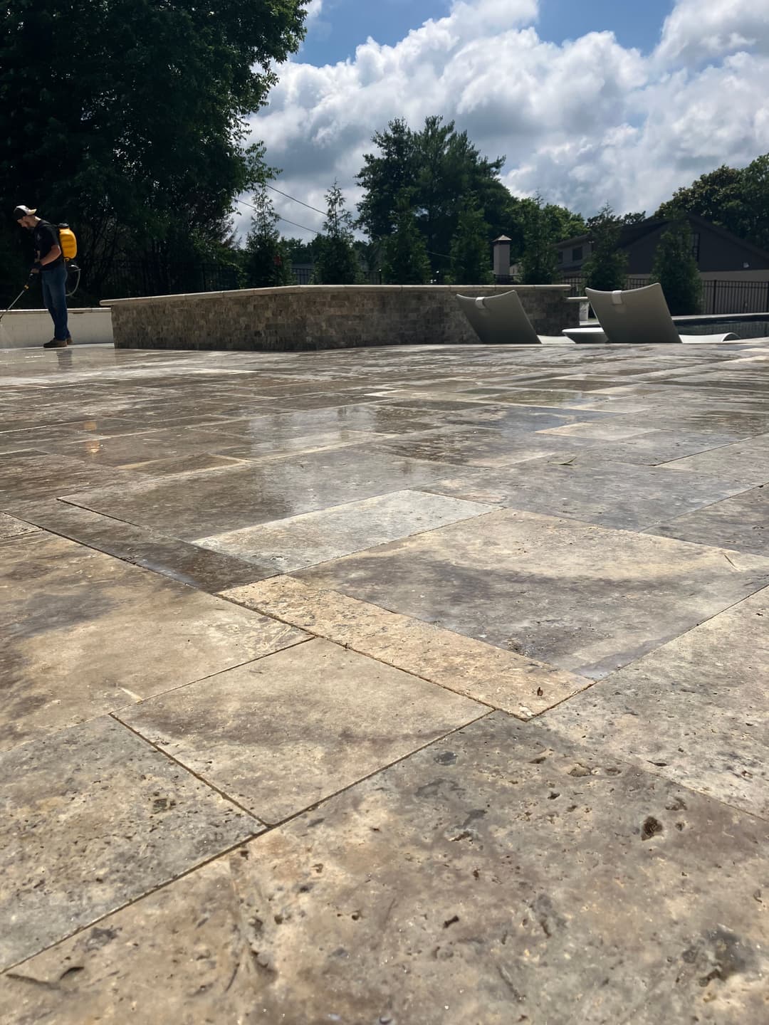 Polished stone patio with a pool, surrounded by greenery and a worker in the background.
