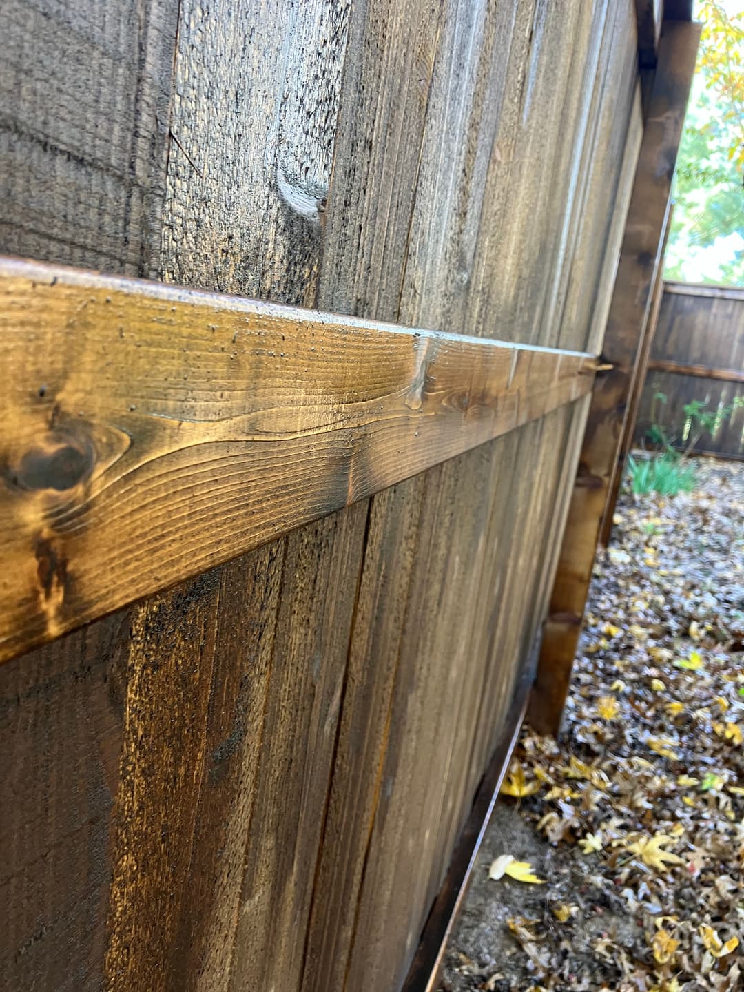Close-up of a wooden fence with horizontal support beams and autumn leaves in the background.