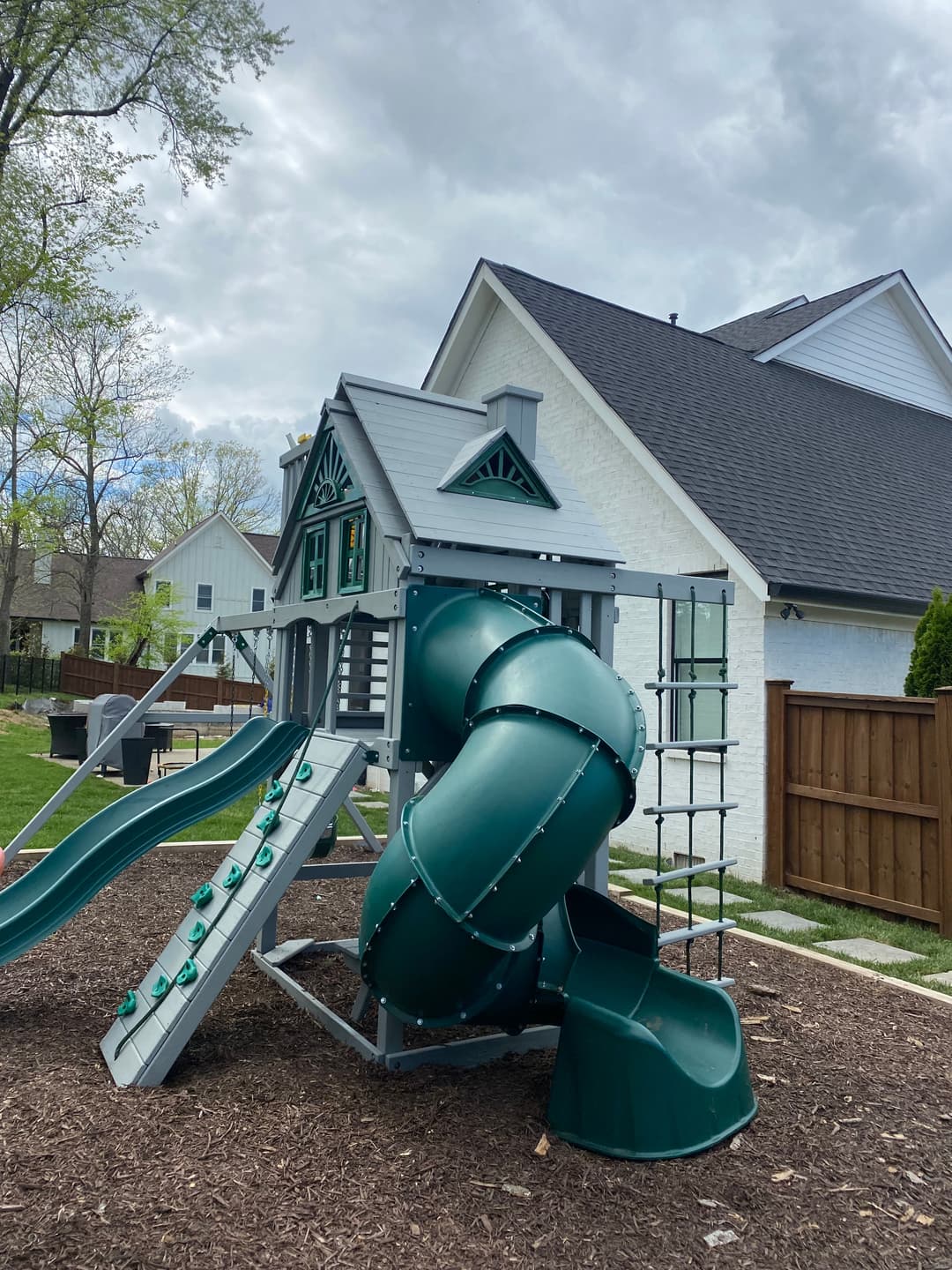 Playground with green slides and twisty slide in a backyard setting.